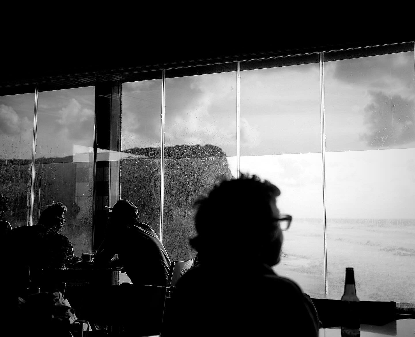 People sitting and enjoying a view of the ocean through large windows from an indoor setting.