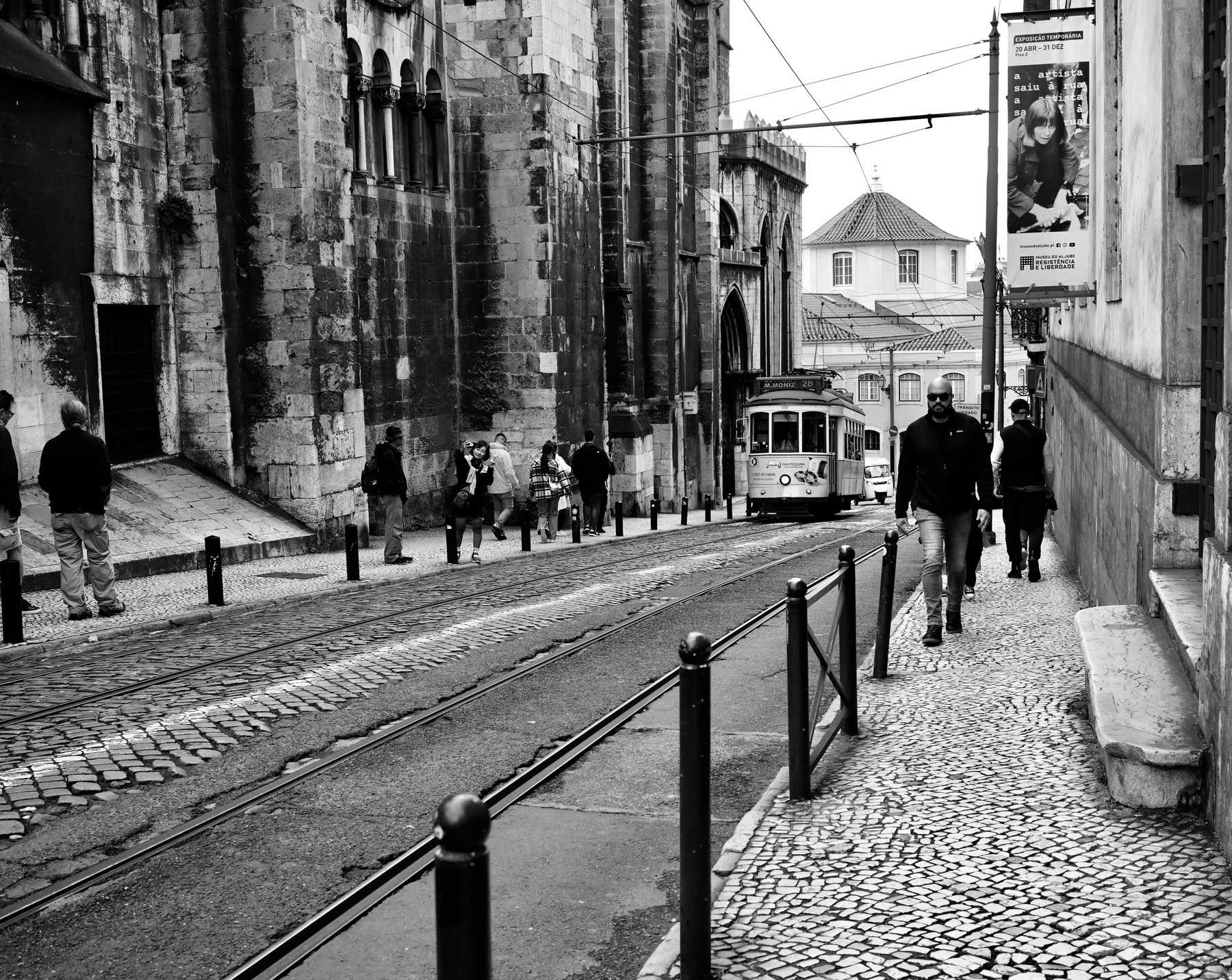 A street scene in black and white features a tram traveling along tracks, surrounded by pedestrians and historic architecture.